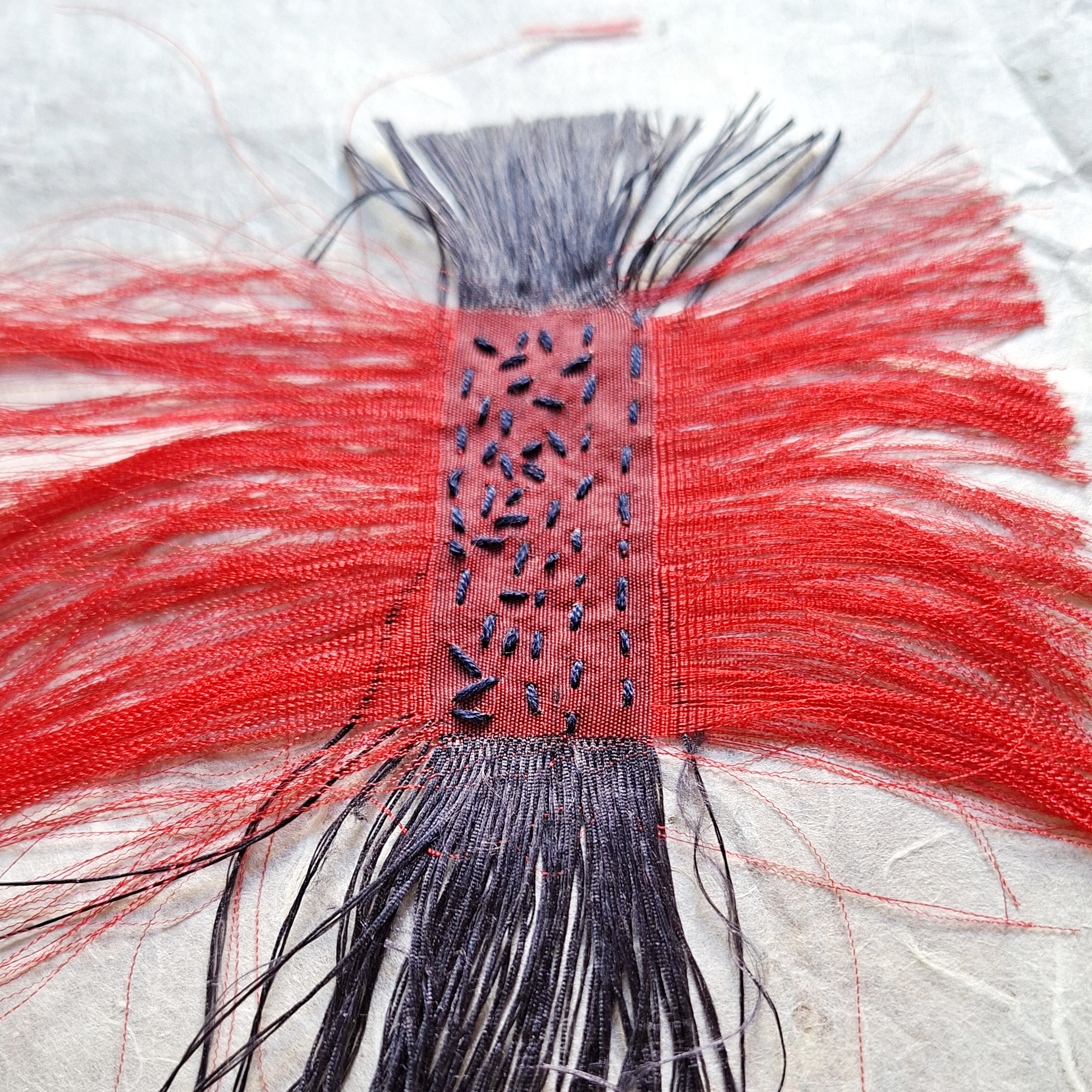 Broderie réalisée à la main sur une chute de soie rouge lors de la création de l'œuvre Murmure.